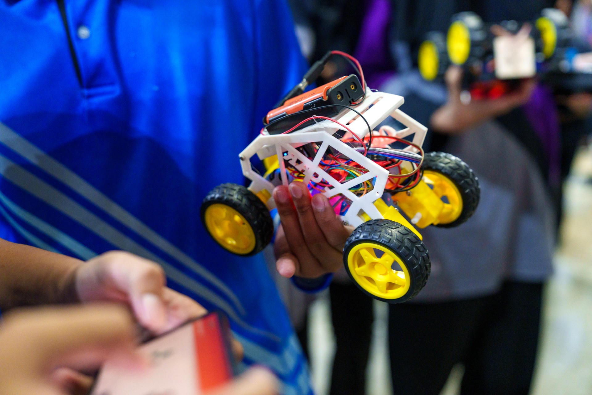 The close-up view showcases a student holding his DIY robotic car, capturing the essence of coding, technology, robotics, and science.